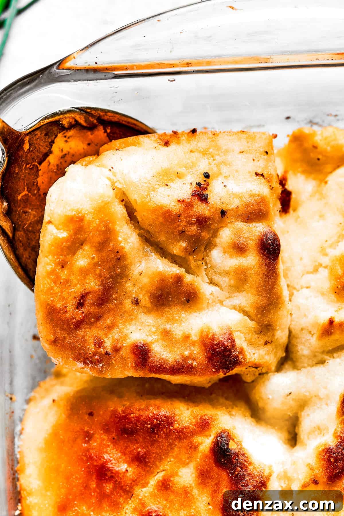 Close-up shot of a serving spoon removing a corner piece from a pan of biscuits.