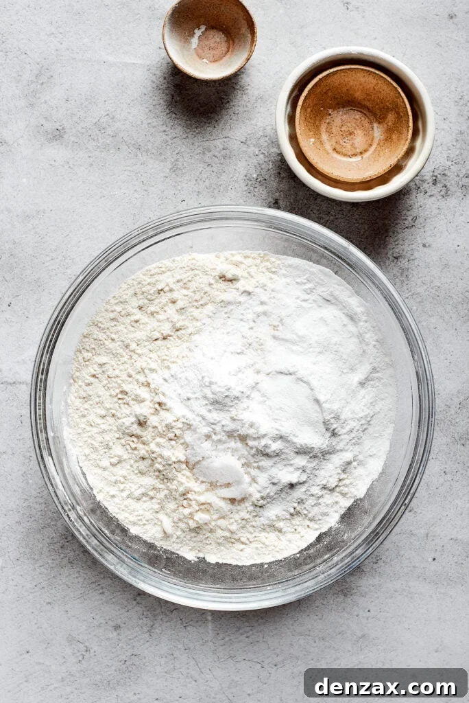 A mixing bowl full of a flour mixture, next to some small and empty bowls