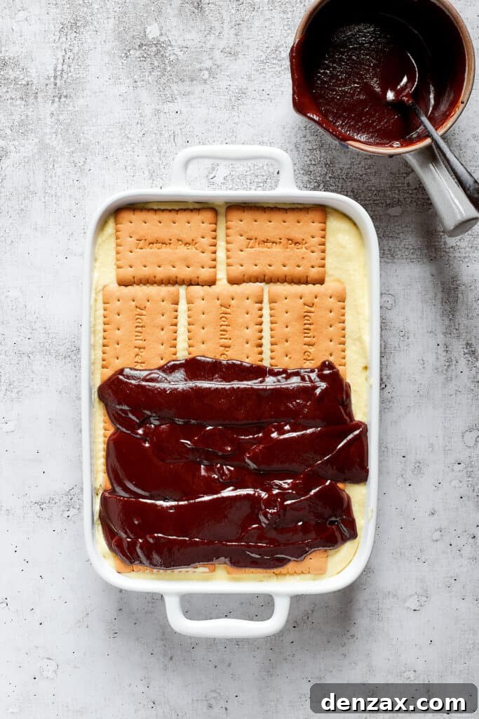 Decadent Chocolate Éclair Cake Recipe — No-Bake Dessert Guide 2 Chocolate ganache half-spread over cookies in a baking dish.