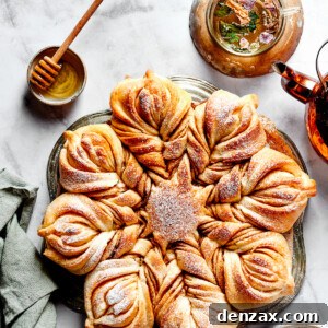Overhead view of a star bread topped with powdered sugar, next to a bowl of honey.