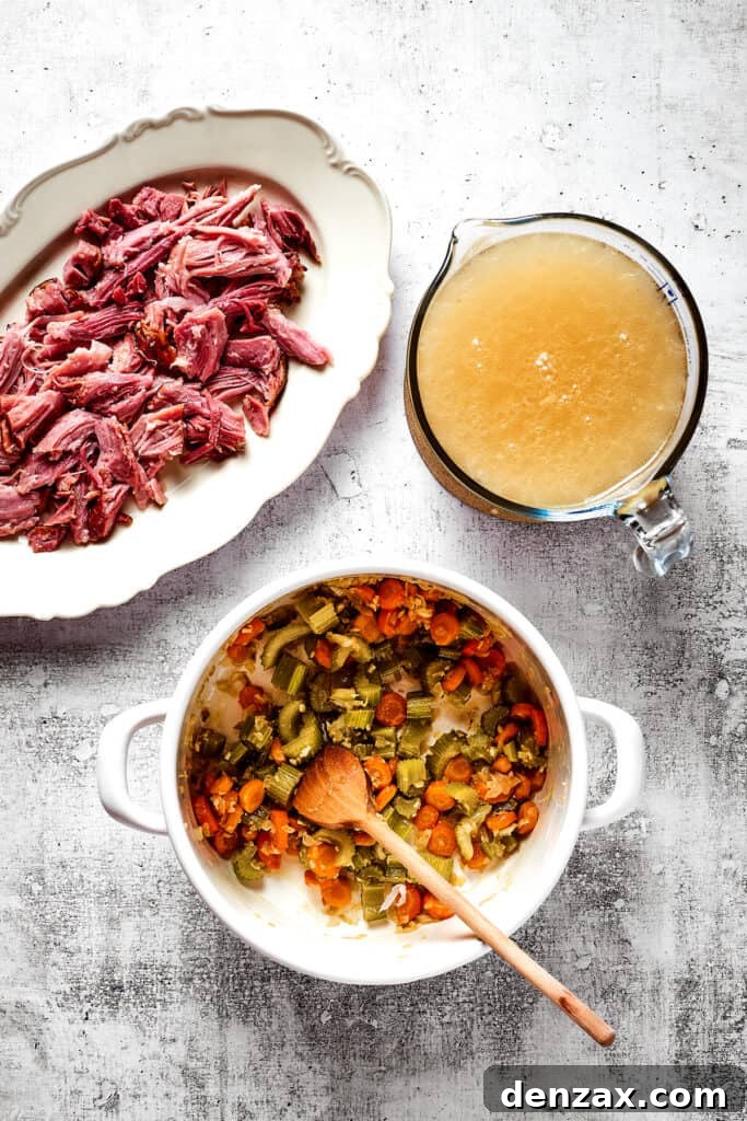 Overhead view of a dutch oven with onions, garlic, celery, carrots, and a wooden spoon, next to a pyrex of broth and a plate of shredded ham.