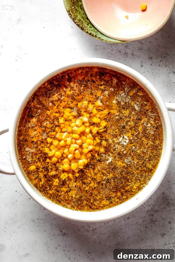 Overhead view of a Dutch oven filled with soup, with corn and white kidney beans on top, next to two empty bowls.