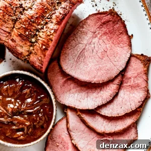 Image of a sliced beef roast served on a white platter with a bowl of gravy set next to it.