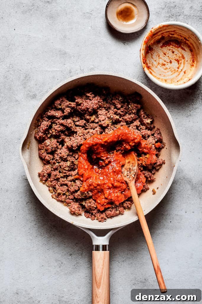 Ultimate Pizza Burger Recipe: How to Make a Cheesy Pizza-Style Burger 2 Pizza sauce is stirred into a pan of browned meat.