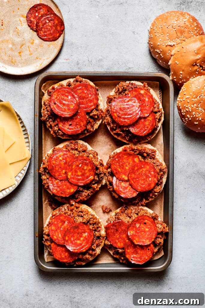 This easy Pizza Burger recipe is sure to become a family favorite! Meat filling is layered with pepperoni and melty mozzarella cheese. Pepperoni is placed on top of pizza burgers on a tray.