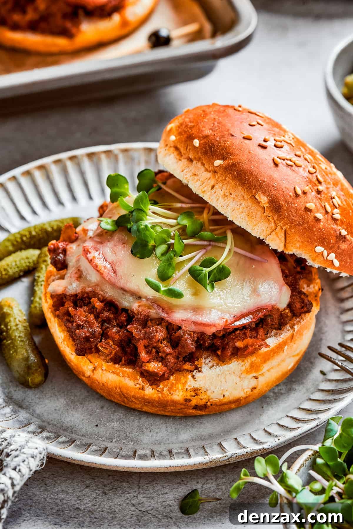 This easy Pizza Burger recipe is sure to become a family favorite! Meat filling is layered with pepperoni and melty mozzarella cheese. Pizza burger with the top bun resting on the side of the burger so the filling is exposed.