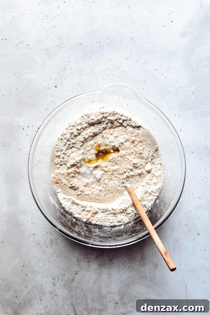 A glass bowl of soft pretzel dough with a wooden spoon.