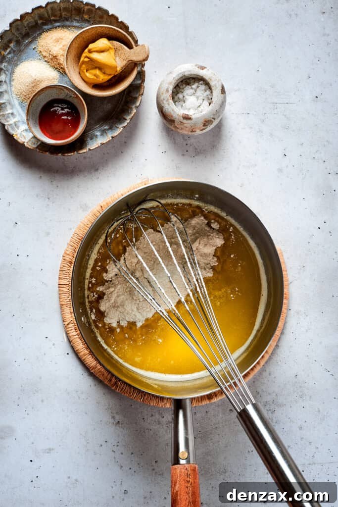 A whisk whisks a cheese sauce in a metal pot.