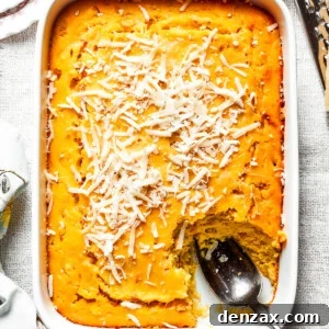 Creamy Corn Soufflé Recipe with Cheesy Golden Top 2 A white baking pan of baked corn souffle with a piece cut out and a spoon in the lower right side.