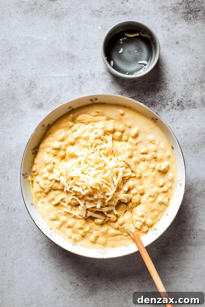 Corn Souffle is rich, creamy, and slightly sweet-savory. It's easily made with pantry and fridge staples, making it a great side dish. Cheese is added to a bowl of corn souffle base.