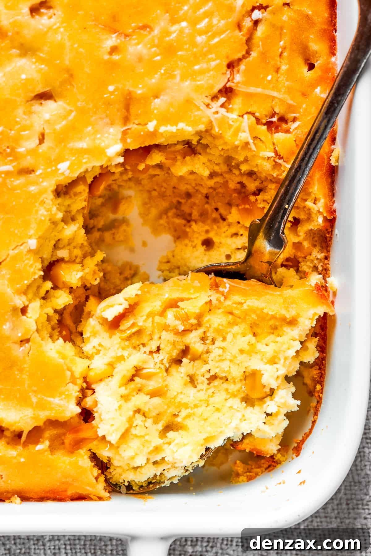 Corn Souffle is rich, creamy, and slightly sweet-savory. It's easily made with pantry and fridge staples, making it a great side dish. Close up image of a spoon taking out a large bite of corn souffle.