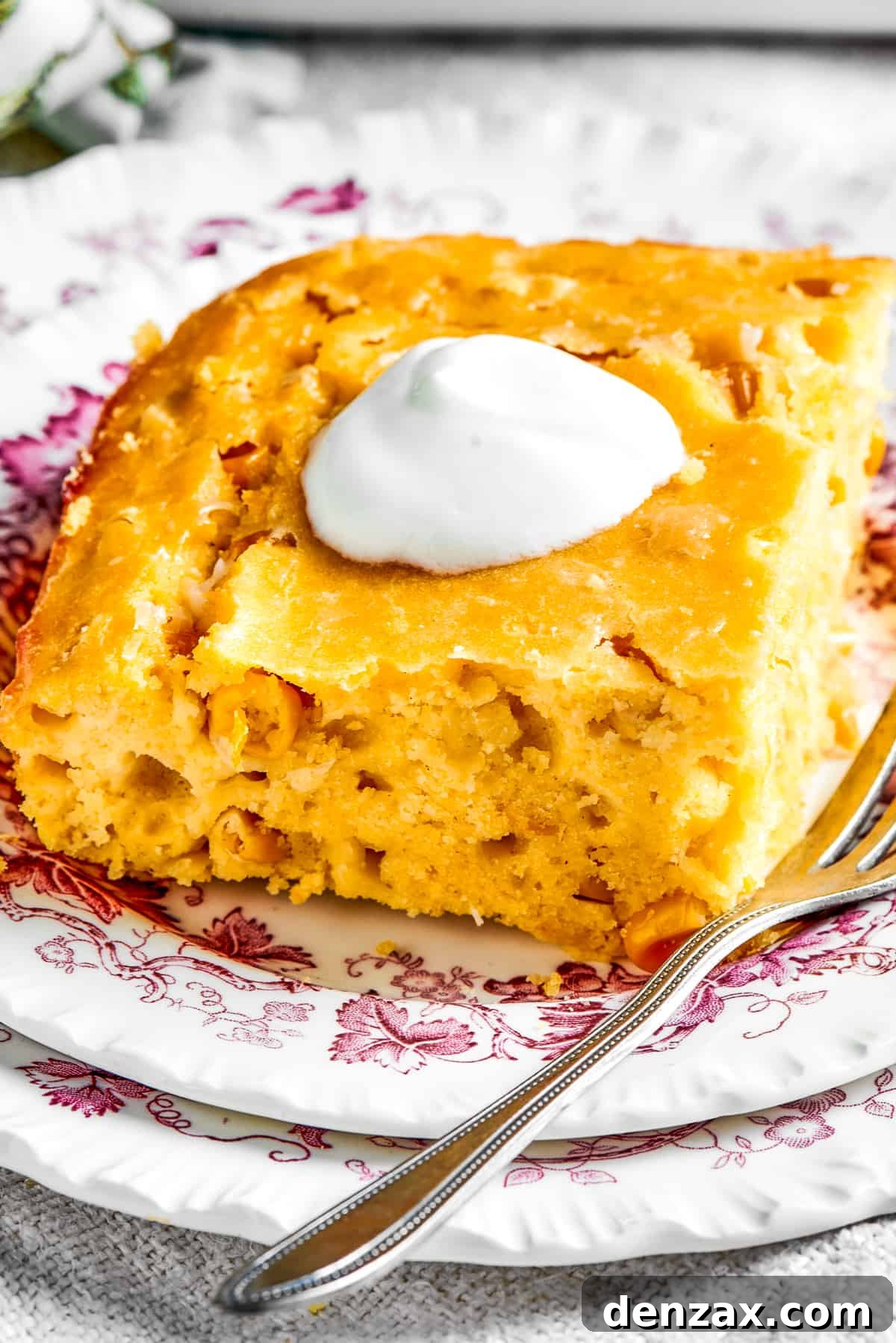 Corn Souffle is rich, creamy, and slightly sweet-savory. It's easily made with pantry and fridge staples, making it a great side dish. Square of corn souffle served on a dish and garnished with a dollop of sour cream.