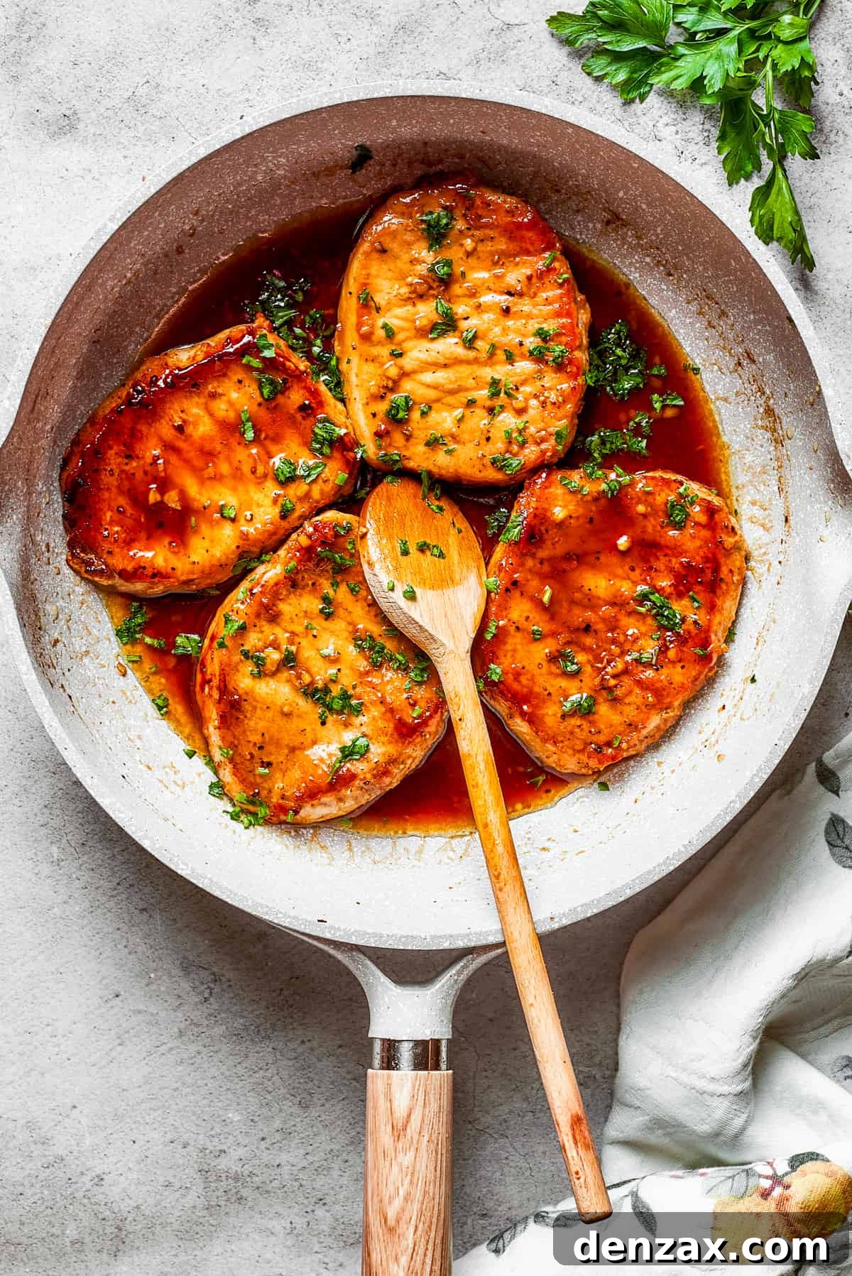 These Honey Garlic Pork Chops are the perfect blend of sweet-salty with a punch of extra flavor from minced garlic. Ready in 20 minutes! Four honey garlic pork chops cooking in a skillet with a wooden spoon stirring through.