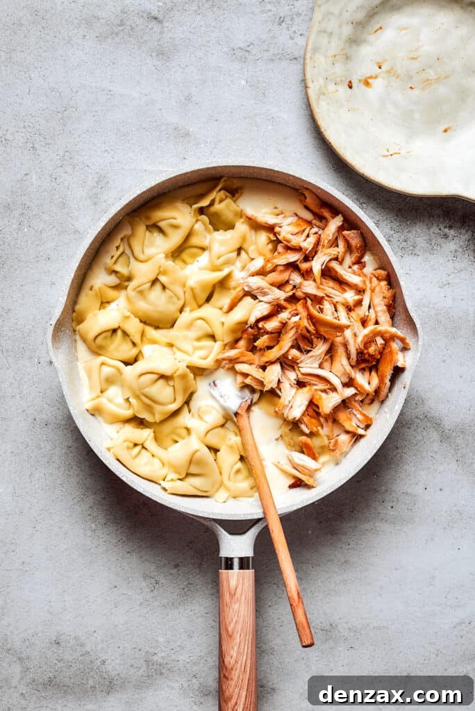 Creamy Chicken Tortellini Alfredo is ready in less than 30 minutes! Rotisserie chicken and tortellini in a cheesy sauce make an easy meal. Cheese tortellini and shredded rotisserie chicken are stirred with a wooden spoon into a skillet of cream sauce.