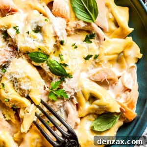Creamy Chicken Tortellini Alfredo Recipe for Dinner 2 A blue bowl with a fork holds a creamy portion of chicken tortellini garnished with parmesan cheese and basil leaves.