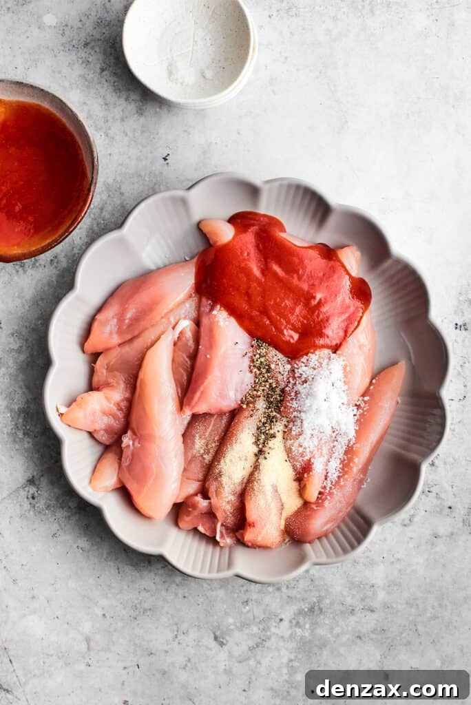 Chicken tenders and seasonings rest in a scalloped white baking dish.