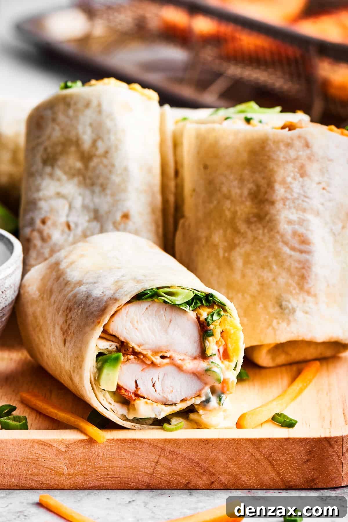 Sliced buffalo chicken wraps are displayed on a wooden cutting board with a bowl of ranch dressing nearby.