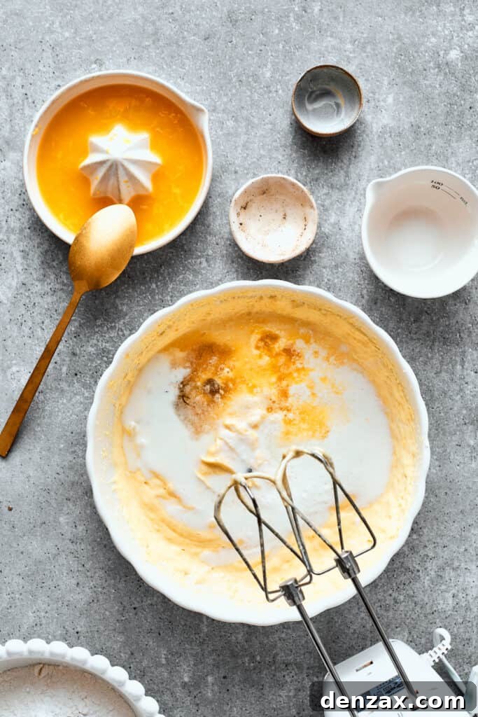Vanilla paste and orange juice are mixed into a bowl of orange cake batter.