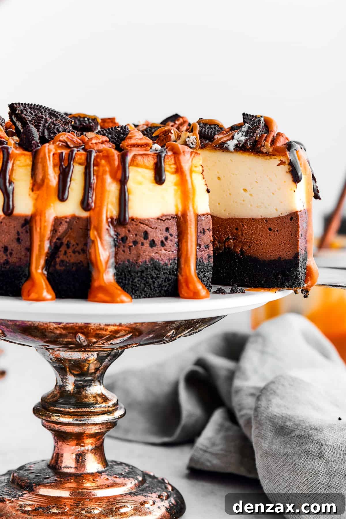A slice of turtle cheesecake is slightly pulled out of the whole cheesecake on the cake stand.