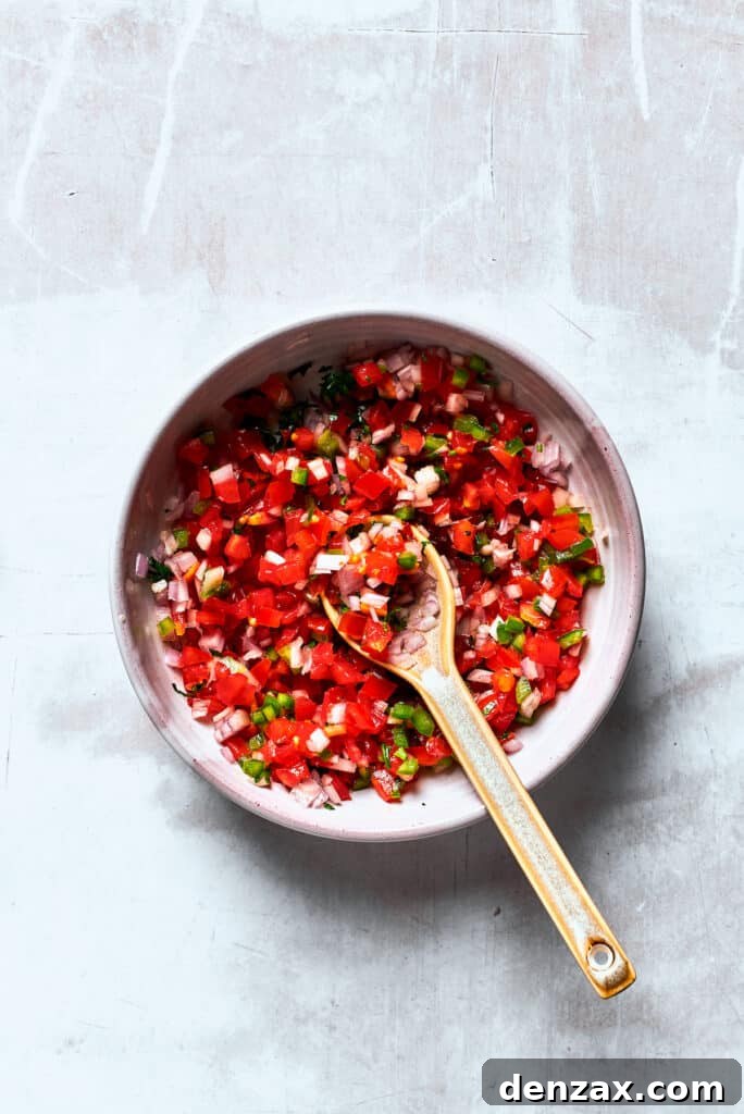 Steak Nachos are piled with homemade guacamole, cheese, pico de Gallo, and juicy steak for a fun twist on nachos. A bowl of Pico de Gallo is mixed with a wooden spoon.