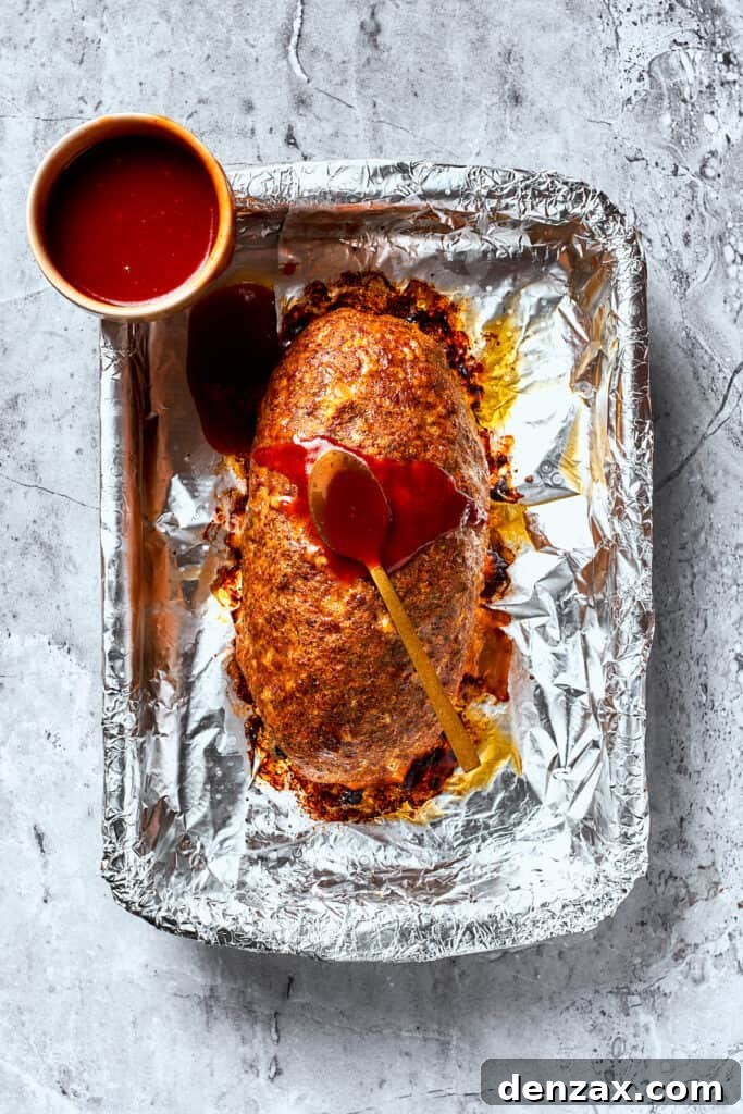 A brown sugar glaze is added to meatloaf on a foil lined pan.