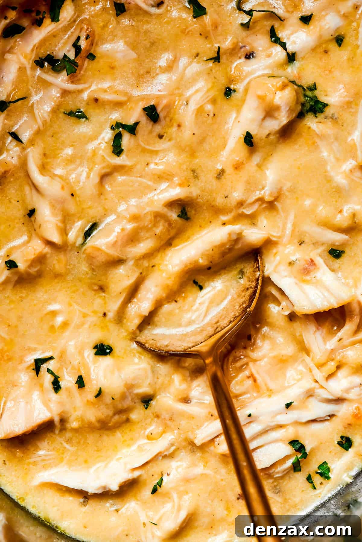 Spoon stirring through creamy sauce and shredded chicken.