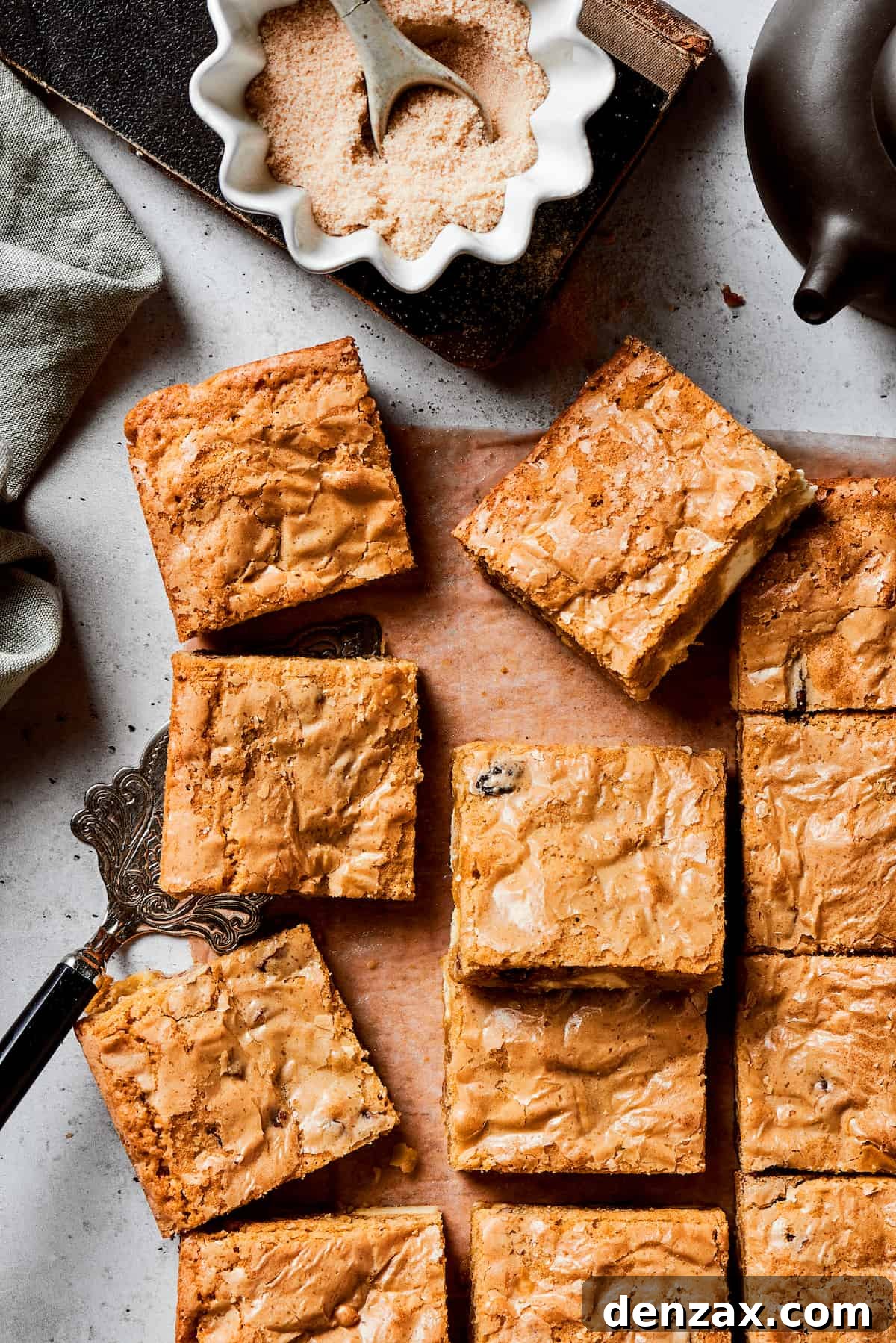 A cutting board of blonde brownie squares with a bowl of brown sugar next to it.