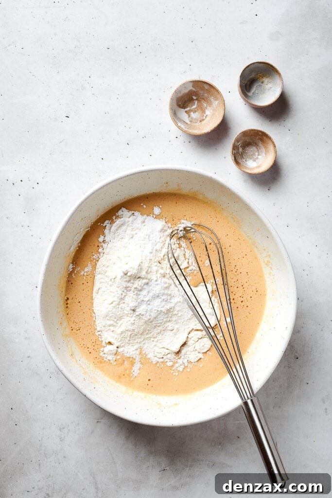 The dry mix is added to the top of a bowl of blonde brownies batter.