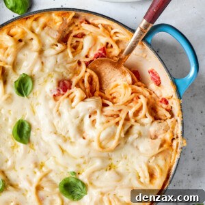 Basil is used as a garnish on a pot of cheesy chicken spaghetti with a serving spoon inserted into the pot.