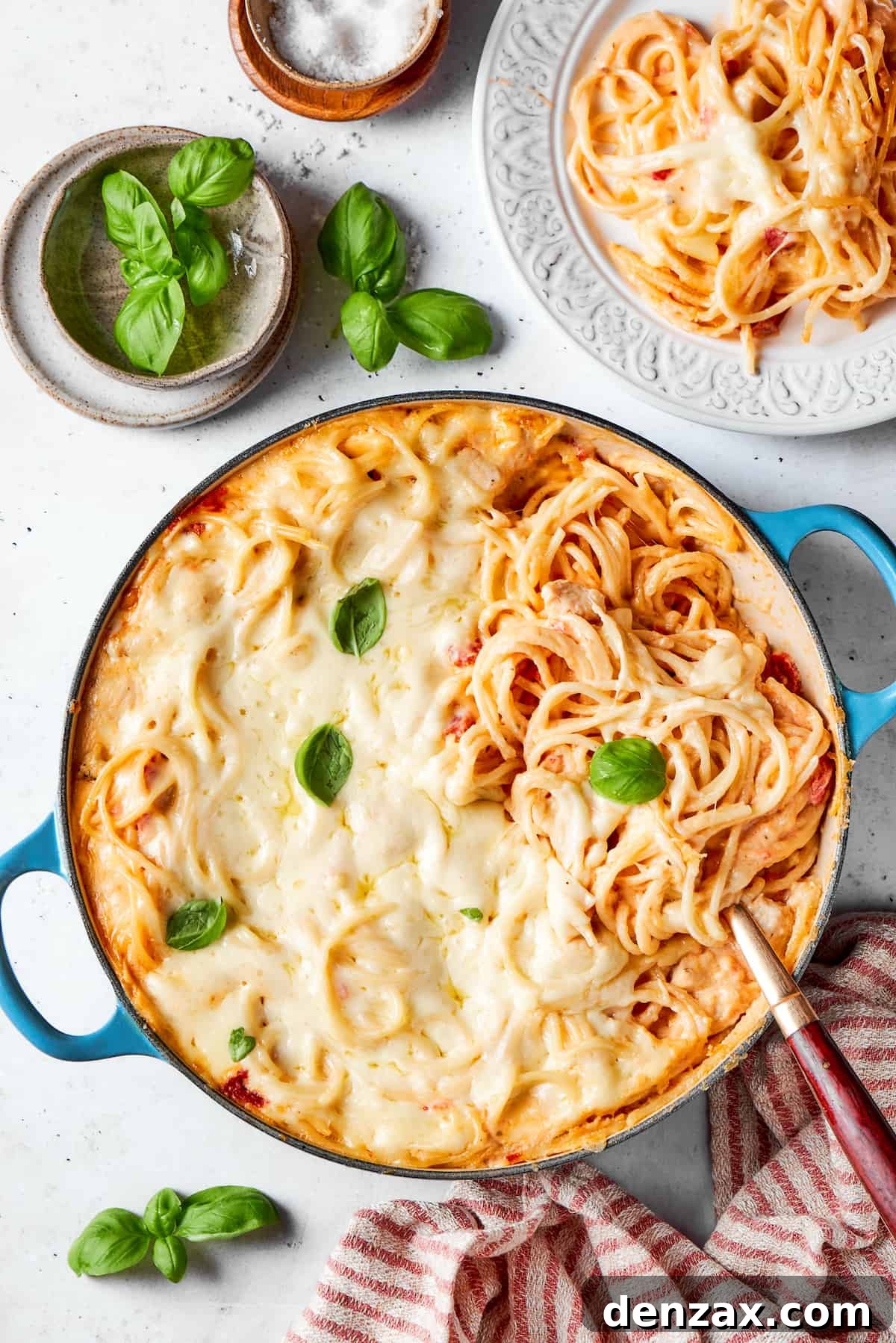 A pot of cheesy chicken spaghetti with a bowl of fresh basil nearby.