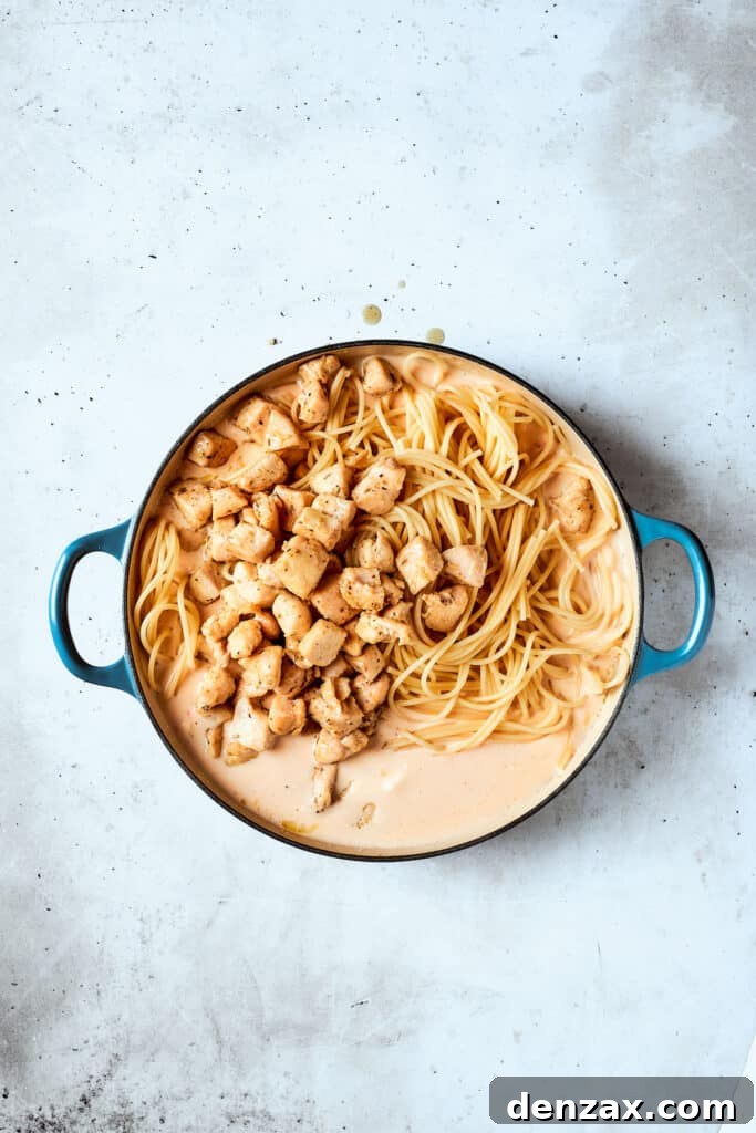 Cooked chicken and spaghetti being added to the sauce.