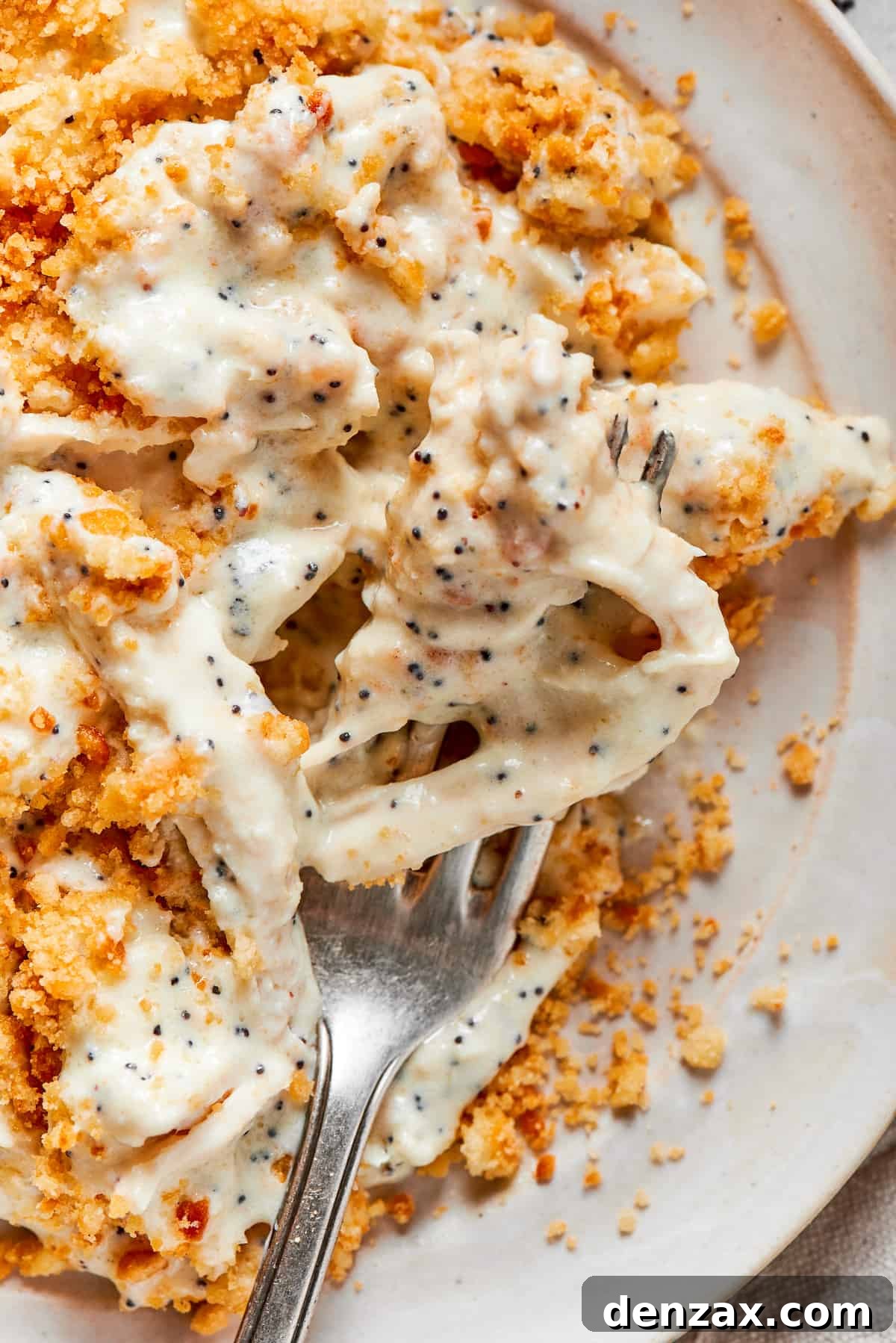 Serve warm with your favorite sides. A fork shows a chunk of poppy seed chicken above a plate of the dish.