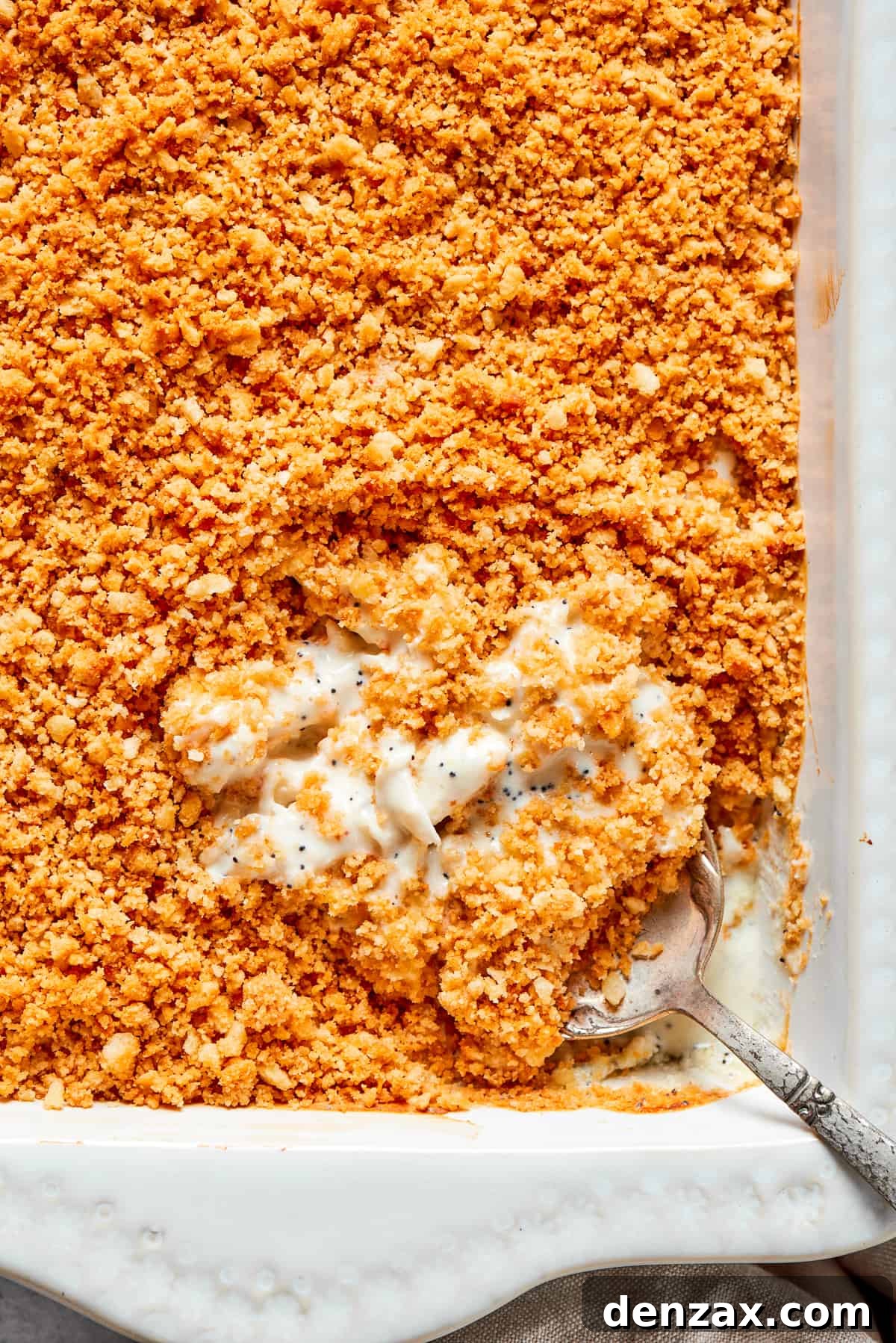 Golden cracker topping and creamy filling make a comforting casserole. A serving spoon digs into a dish of poppy seed chicken topped with crushed Ritz crackers.