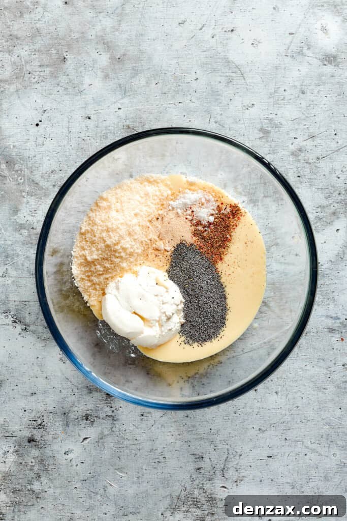 Mix the sauce ingredients together. Sour cream, parmesan, cream of chicken soup, spices, and poppy seeds are combined in a bowl.