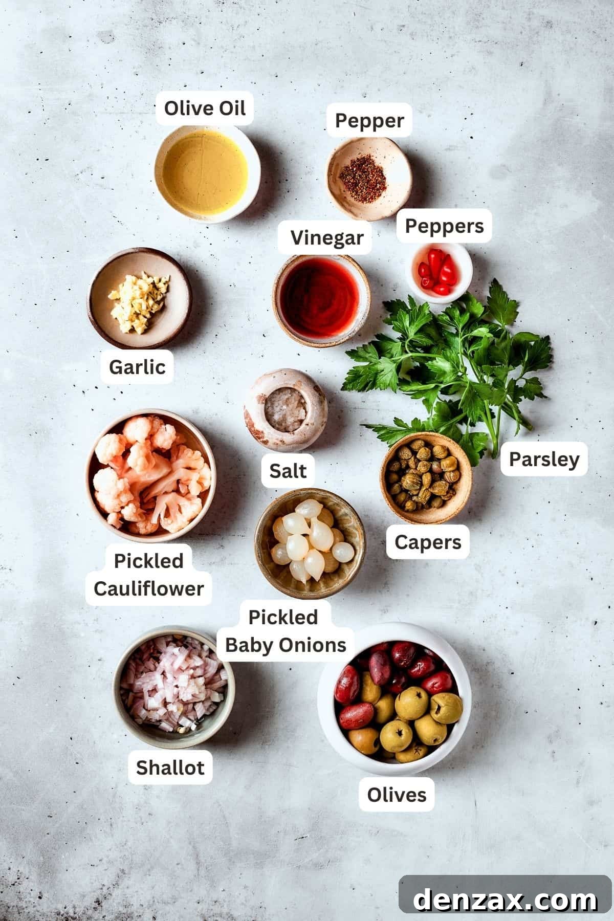 The ingredients for olive salad are shown: olives, peppers, pickled cauliflower, vinegar, parsley, capers, pickled baby onions, garlic, olive oil.