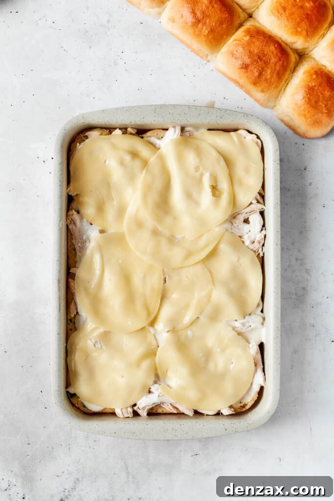 Chicken Bacon Ranch Sliders feature tender bites of shredded chicken, crisp bacon Ranch dressing, melted cheese, and sweet rolls. Provolone placed on sliders.