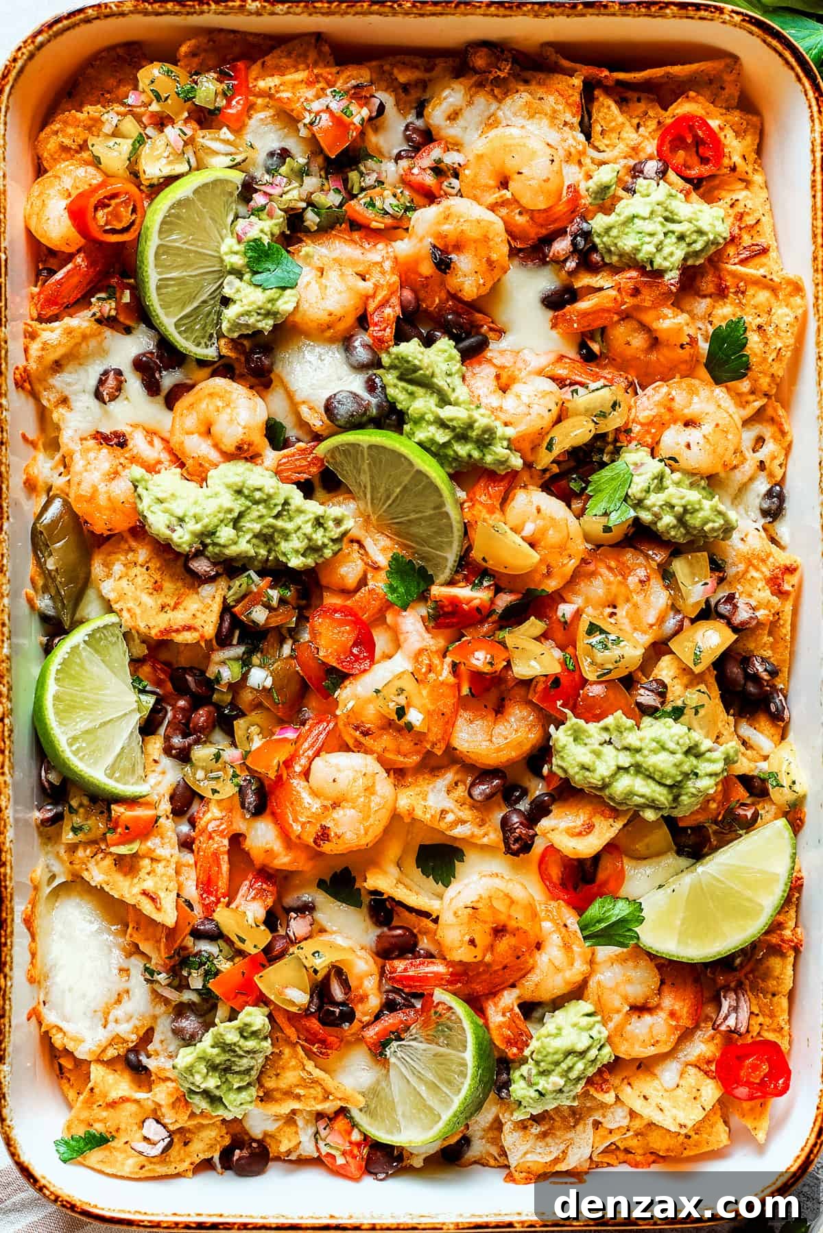 Nacho chips topped with shrimp, cheese, black beans, tomatoes, and a garnish of guacamole and slices of lime.