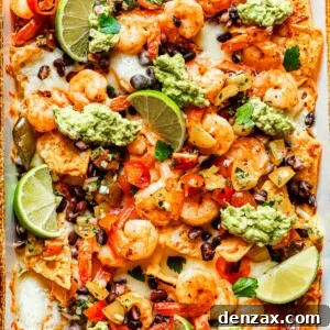 Nacho chips topped with shrimp, cheese, black beans, tomatoes, and a garnish of guacamole and slices of lime.