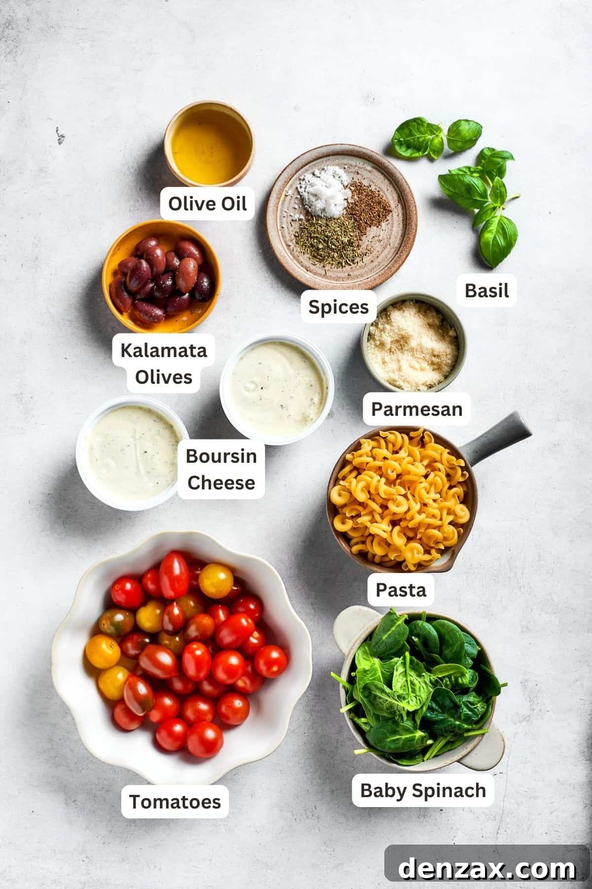Ingredients needed to make Boursin pasta are shown: Boursin cheese, cherry tomatoes, grape tomatoes, Parmesan, Kalamata olives, pasta, baby spinach, basil, Italian seasoning, olive oil, salt and pepper.