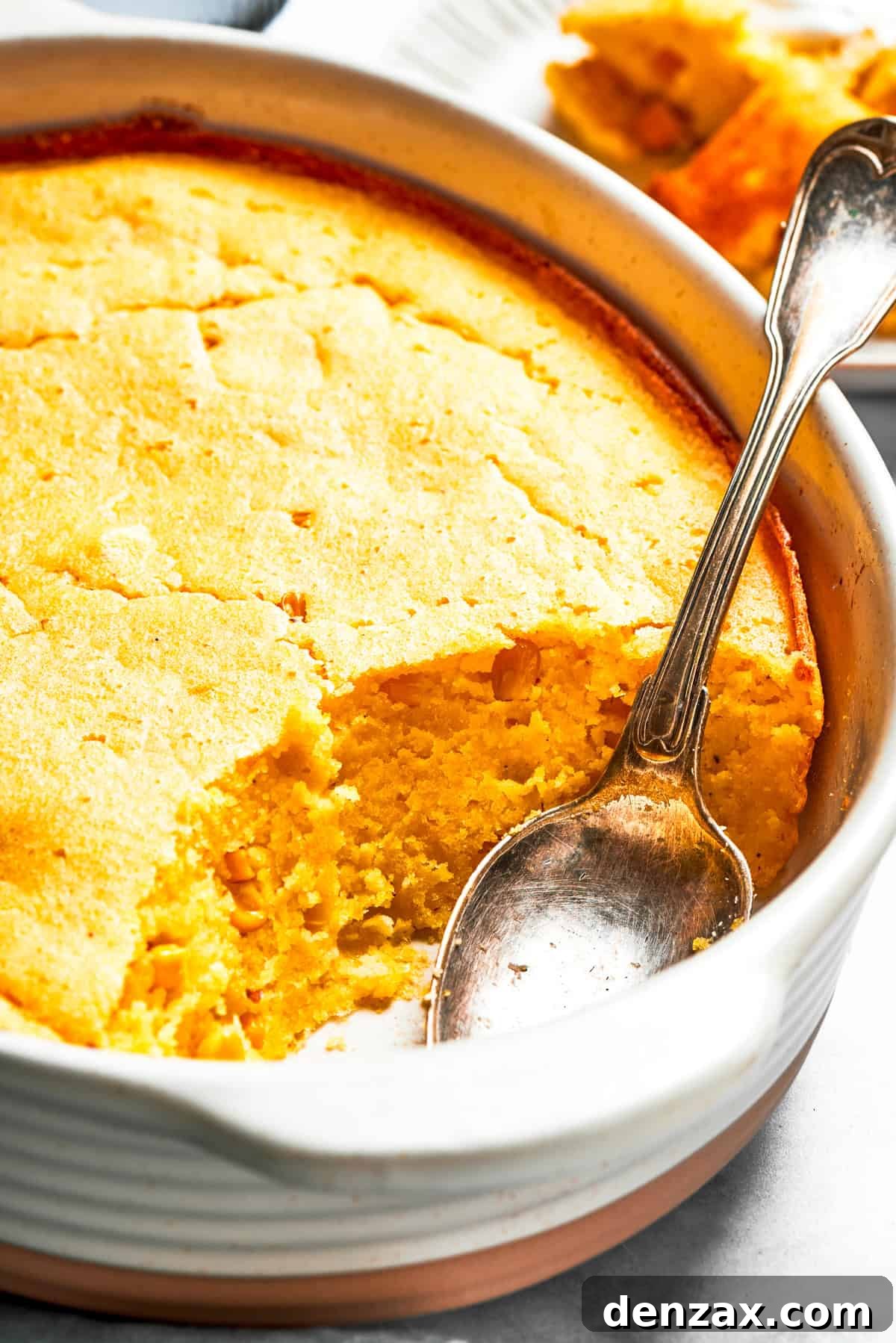 Spoon bread in a casserole dish with a spoon placed inside it.