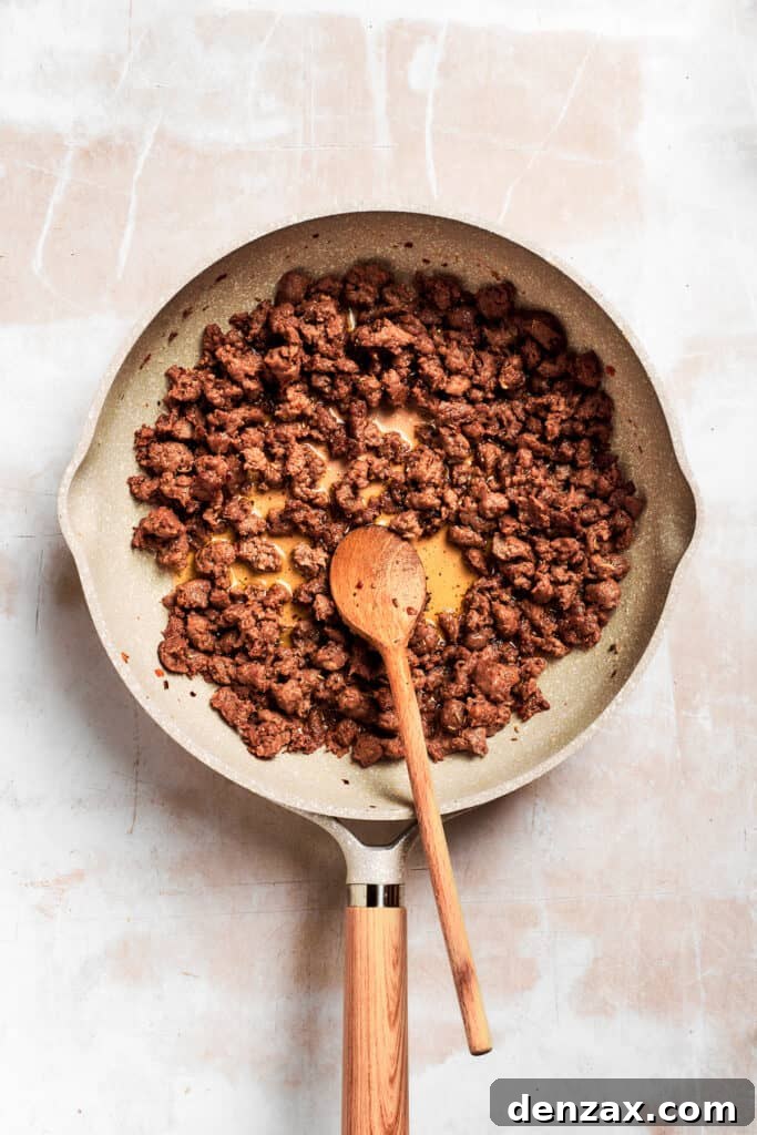 A wooden spoon stirs the pan of sausage.