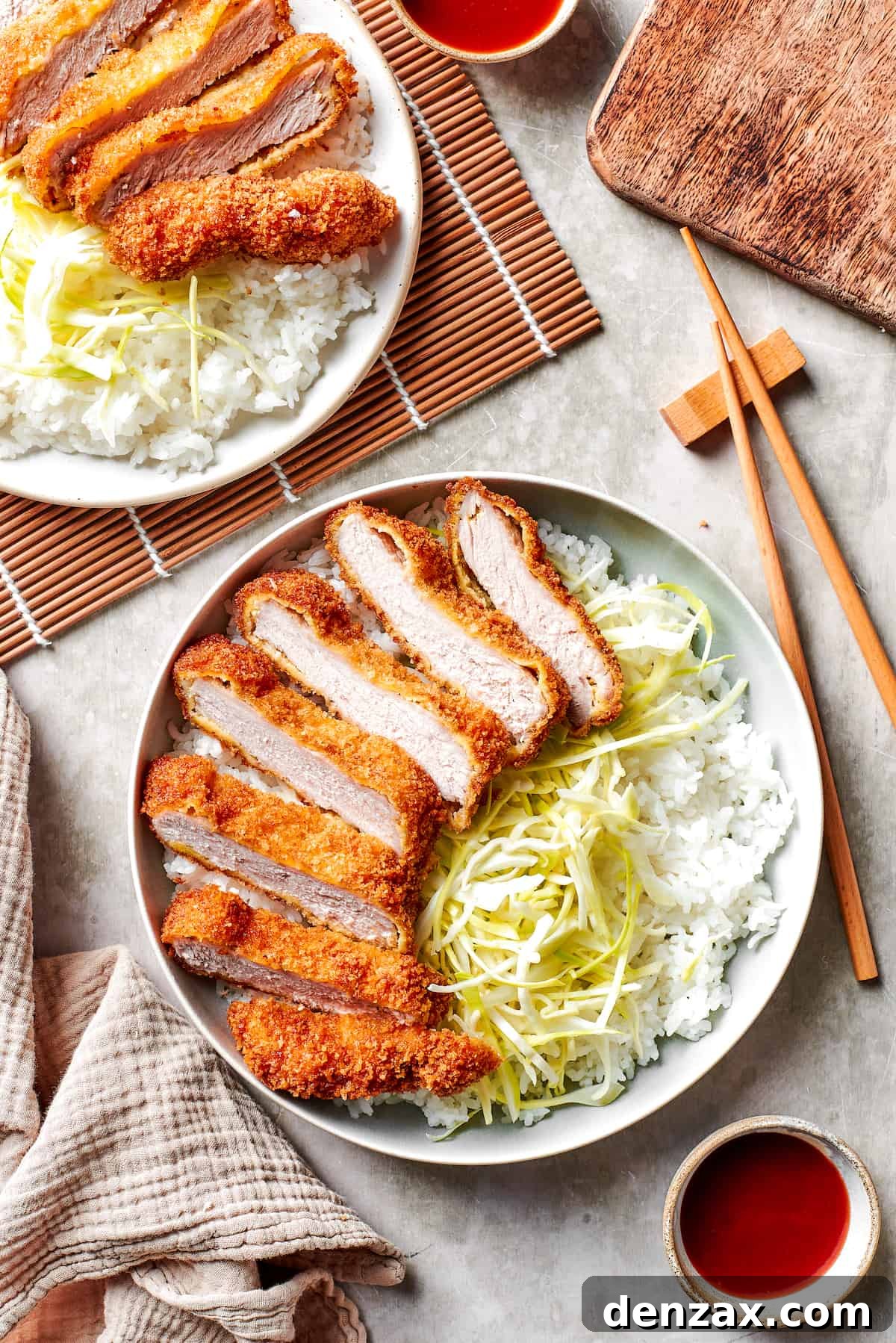 Japanese Tonkatsu sliced and served over cabbage and rice on dinner plates.