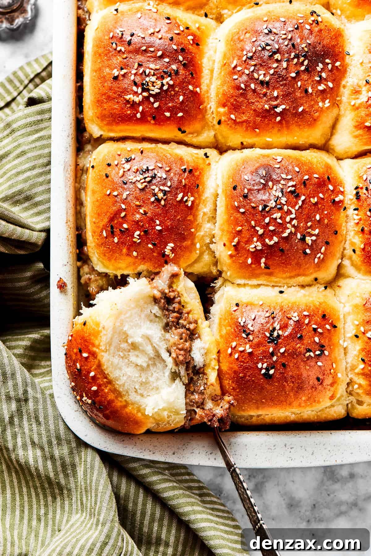 Finished cheeseburger sliders. Cooked sliders in a baking dish, with one slider facing up so its filling is exposed.