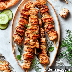 A platter of grilled chicken souvlaki on skewers surrounded by herbs and cucumber slices.