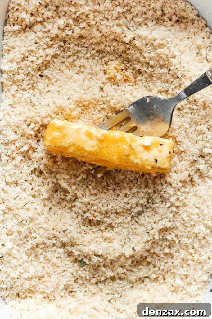 A fork tosses the piece of mozzarella in breadcrumbs.