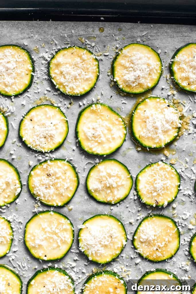 The zucchini chips are spread out on a lined baking sheet.