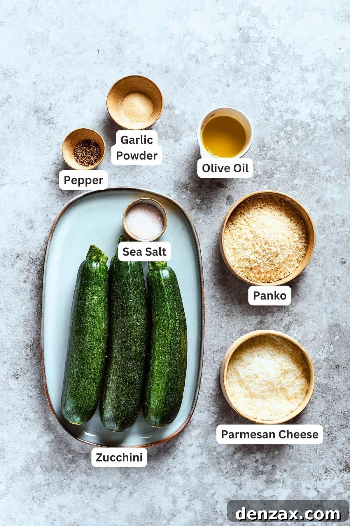 Ingredients for zucchini chips are shown labeled and portioned out: zucchini, garlic powder, pepper, olive oil, panko, salt, parmesan cheese.