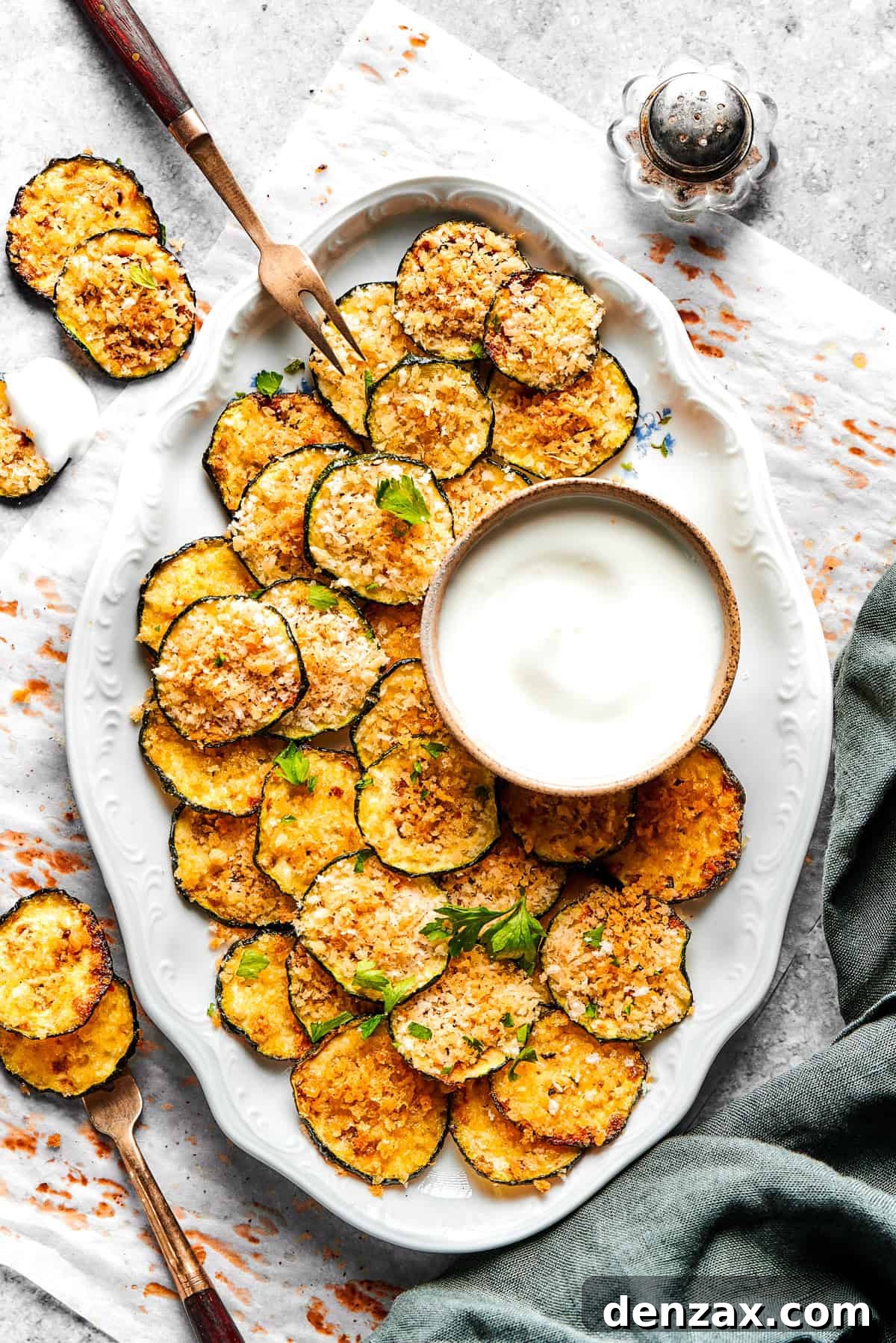Baked zucchini chips served on an oval white platter with a bowl of dip.