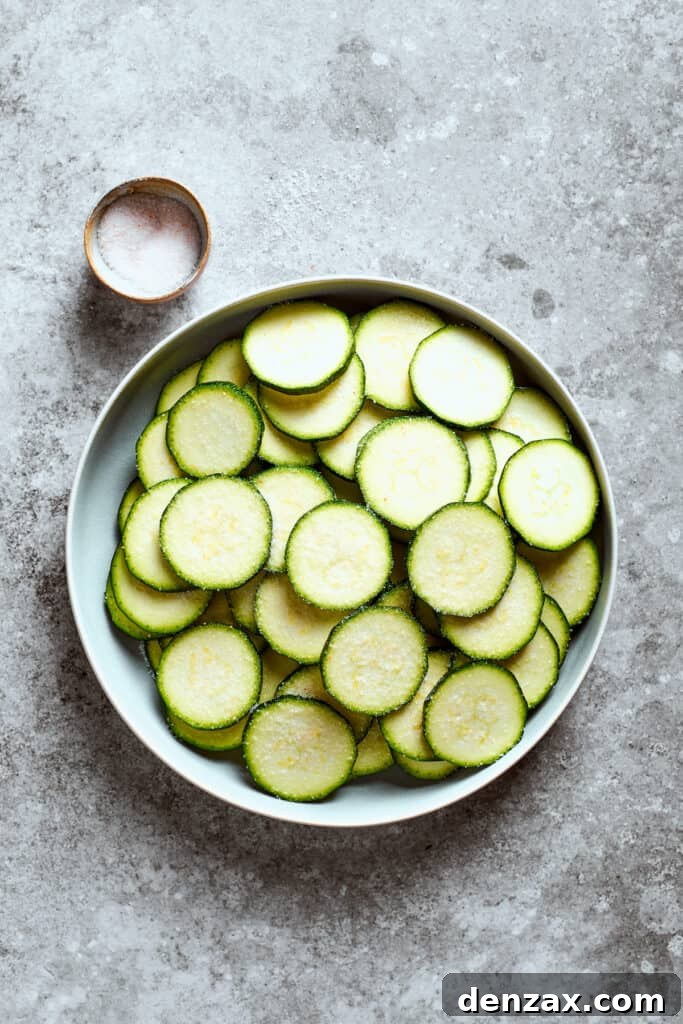 A bowl of sliced zucchini next to a small bowl of salt.