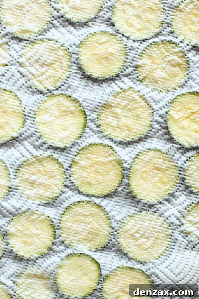A paper towel covers a baking sheet of zucchini slices.